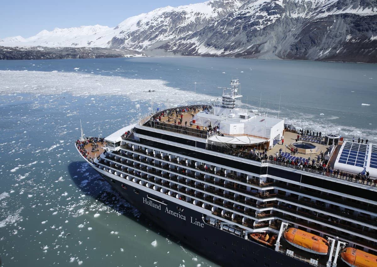 Holland America Line cruise ship sailing in Alaska with a snow covered mountain and icy ocean in the background.