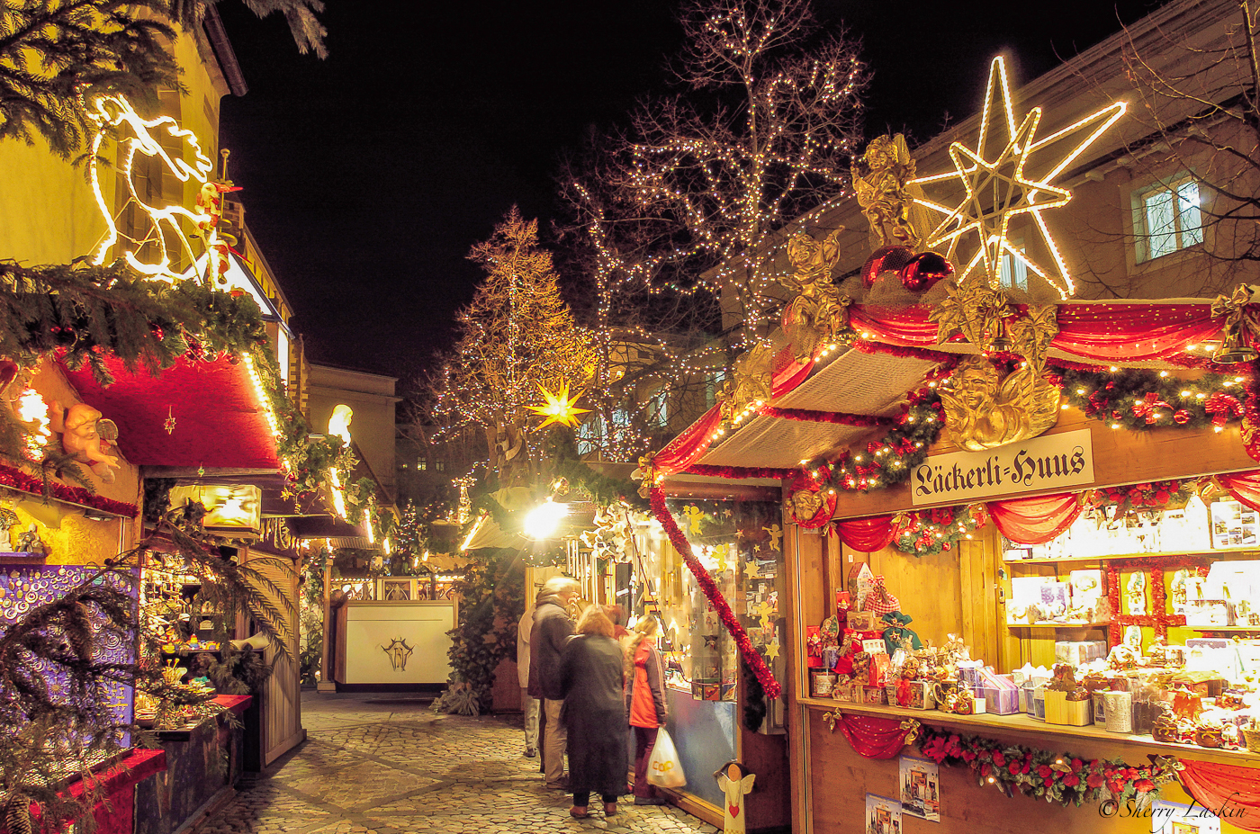 Christmas markets brightly lit stalls with people browsing over decorations.
